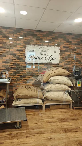 Burlap sacks of green coffee stacked under a Coffee Bar sign on a brick wall