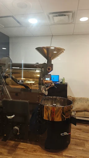 A drum coffee roaster with a copper hopper and cooling tray in the back room