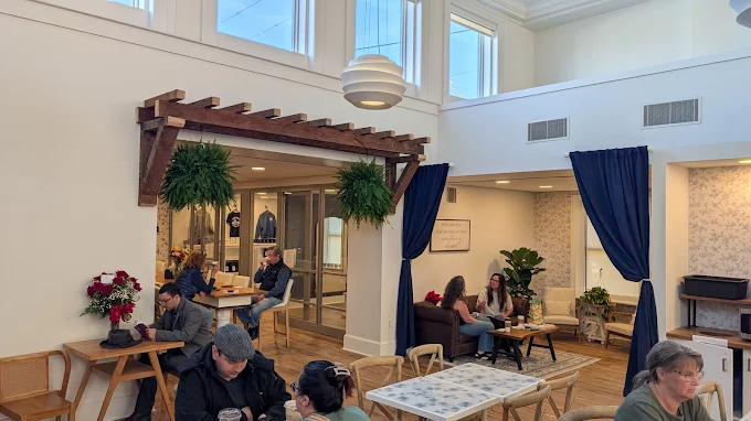 The tall main room with pendant lights, high windows, a wooden pergola, and people at tables